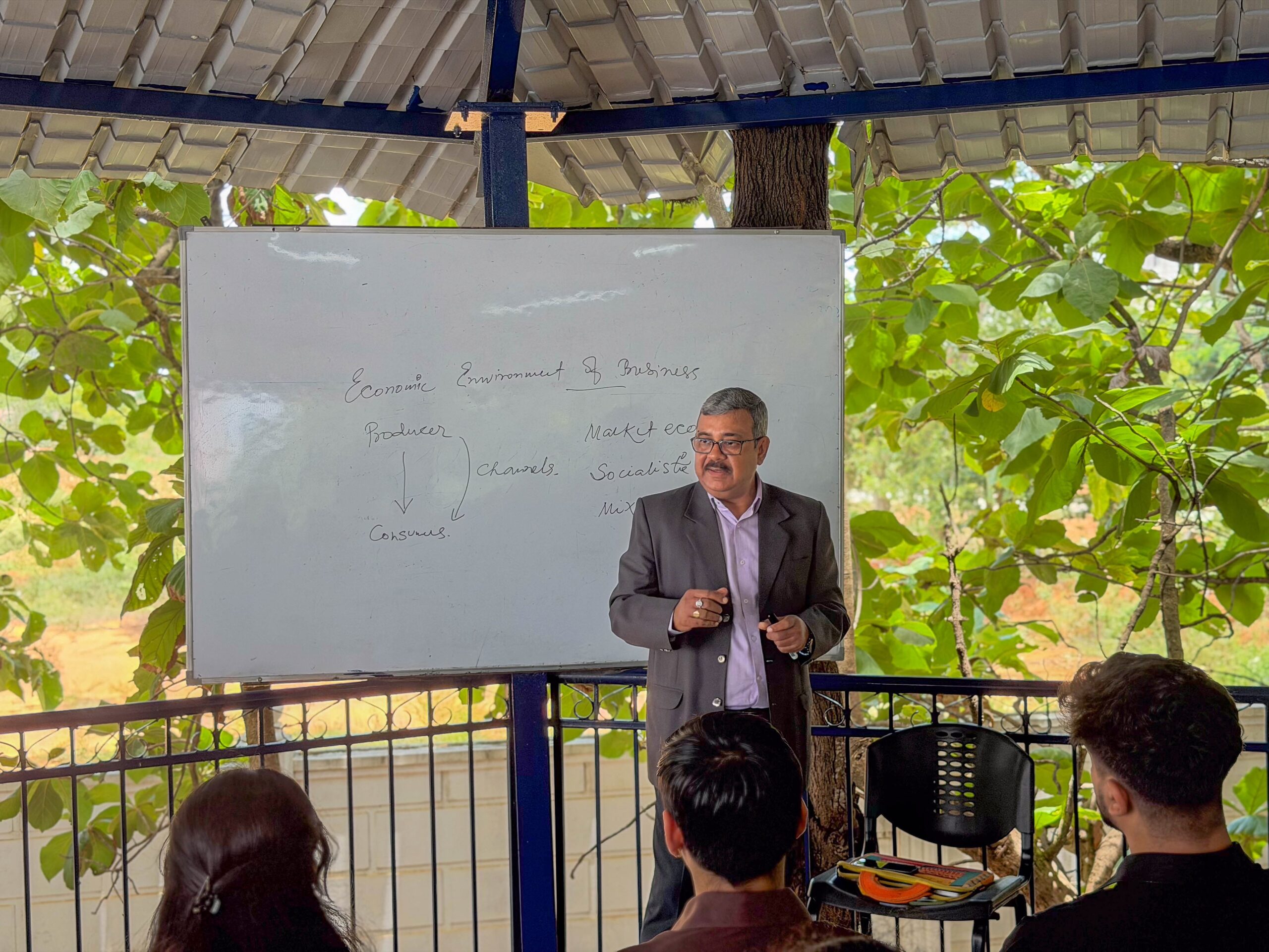 RCMB faculty teaching business concepts at a whiteboard in an open-air pavilion